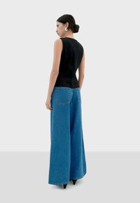 Schwarzes, tailliertes Oberteil mit ärmellosem Design, kombiniert mit hoch taillierten blauen, weitem Jeanshosen. Glatte Texturen, minimale Nähte und übergroße Taschen.