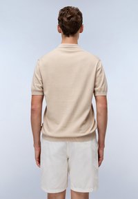 Maglione in cotone beige a maniche corte con colletto a polo e orlo a costine, abbinato a pantaloni corti bianchi. Texture liscia, design semplice, senza motivi visibili.