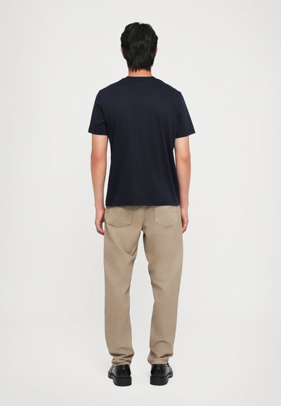 T-shirt bleu marine à col ras du cou associé à un pantalon beige ; le tissu semble lisse, avec une coupe décontractée et des poches arrière visibles sur le pantalon.