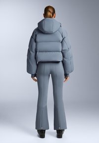 Siva puffer jakna s kapuljačom, s krojenim siluetom, qiltiranim teksturom i širokim rukavima, u kombinaciji s pripijenim hlačama istog materijala.