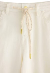 Bílé lehké kalhoty z texturované látky, s tlustým provazovým páskem v pase a akcenty z pozlaceného kovu.