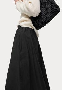 Gonna nera a pieghe con una texture morbida e una vita elastica, abbinata a un maglione di maglia crema e una borsa nera intrecciata.