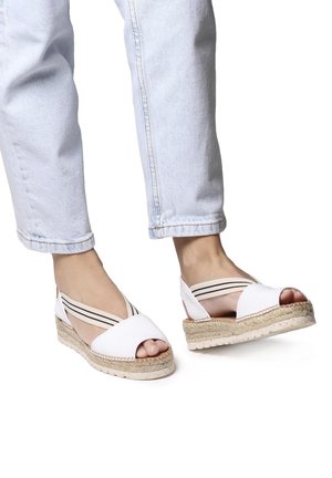 Sandali espadrille bianchi con punta aperta, cinturini elastici bianchi e neri e suola in corda intrecciata naturale. Indossati con jeans a 3/4 blu chiaro.