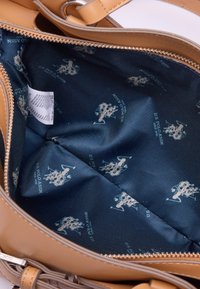 L'interno della borsa sintetica marrone presenta una fodera in tessuto blu con un motivo a logo chiaro ripetuto e un'etichetta di cura visibile.
