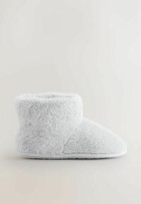 Tekoturkisvalkoinen tohveli, jossa pehmeä pinta, nilkkapitoinen muoto, pyöreä kärki ja tasainen, joustava pohja mukavuutta ja helppoa käyttöä varten.