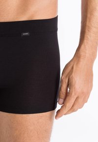 Black cotton boxer shorts with a smooth texture, elastic waistband, and a small logo tag, displaying a fitted design.