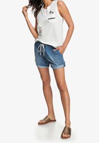 Haut blanc sans manches avec poche imprimée de palmiers, short en jean avec cordon de serrage, et sandales marron à enfiler. Tenue d'été décontractée avec des tissus doux.