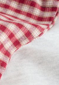 Nærbillede af blødt stof med tern i rød og beige, foldet over ensfarvet hvidt, tekstureret stof.