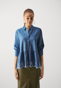 Denimskjorte med knappestolpe foran, krage og trekvart ermer, med broderi av blomsterdesign og en flared, plissert del nederst.
