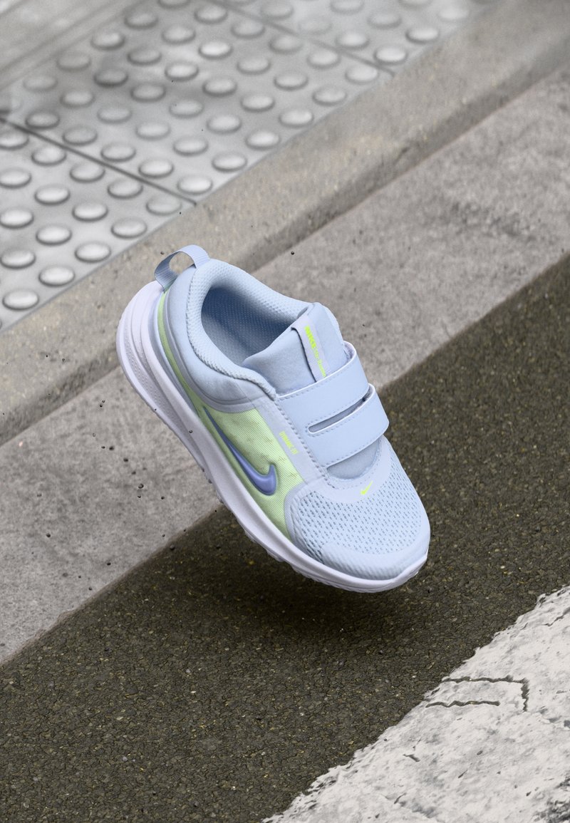 Baskets bleu clair avec tige en mesh, brides Velcro, semelle blanche et accent réfléchissant en néon vert et violet.