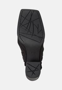 Suola nera della scarpa con un motivo di grip testurizzato, che mostra una sezione di tessuto lungo il lato, enfatizzando funzionalità e stile.