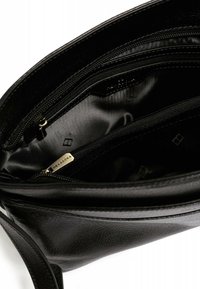 Borsa a mano in pelle nera con una texture liscia, presenta scomparti interni con zip e una sottile placca con logo. Rivestita in tessuto satin nero.
