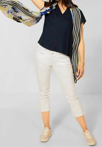 Laivastansininen v-kauluksellinen paita lyhyillä hihoilla, yhdistettynä vaalean beigeihin capri-housuihin ja beigeihin lenkkareihin. Asusteena värikäs kuviollinen huivi.