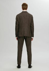 Brauner Tweed-Anzug mit strukturierter Oberfläche, bestehend aus einem Blazer mit zwei Knöpfen und geraden Hosen. Getragen mit schwarzen Schuhen, Rückansicht gezeigt.