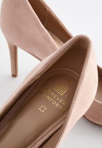 Roosa suede kõrge kontsaga kingad, millel on sujuv, ümar disain. Kuldsed brändimistooted sisetallal; saledad stilettokonts. Pehme tekstuur.