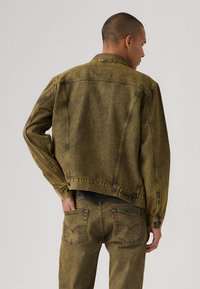 Πράσινο μπουφάν από τζιν σε χαλαρή γραμμή, με κουμπιά μπροστά και λεπτομέρειες σε τσέπη στο στήθος. Διαθέτει αντίθετη ραφή και ξεθωριασμένη υφή.