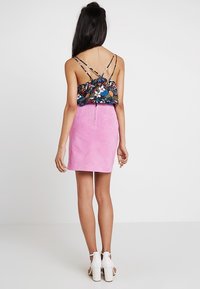 Haut à motif floral avec bretelles ajustables associé à une mini-jupe en suédine rose. Des sandales blanches à talons complètent la tenue.