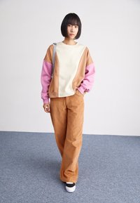 Sweatshirt à blocs de couleurs avec des sections crème, beige et rose ; associé à un pantalon en velours côtelé beige. Texture douce, coupe décontractée et style casual.
