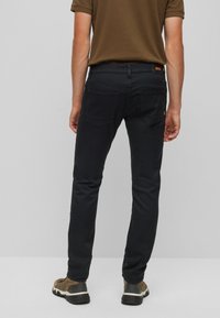 Svarta denimbyxor med slim fit, med bakfickor och en logotypapplikation på midjan. Kombineras med bruna skor.