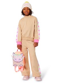 Completo con felpa e pantaloni beige con dettagli rosa; cappello leggero rosa. Lo zaino presenta una fantasia di un gatto con finitura luccicante e colori pastello.
