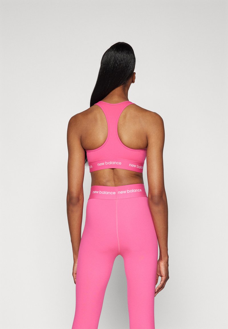 Sostén deportivo rosa y leggings a juego de tejido elástico. El sostén cuenta con un diseño de espalda nadadora y una banda con logo. Textura suave.