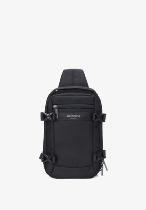 Zaino a spalla in tessuto nero con spallacci regolabili, tasche con zip esterne e fibbie laterali. Presenta il logo sul pannello frontale.