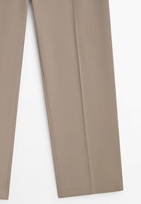 Pantalons beige sur mesure avec jambes droites, plis avant visibles et ourlets cousus sur fond blanc.