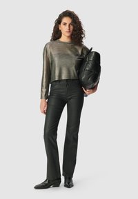 Metallic grauer, kurz geschnittener Pullover mit langen Ärmeln, kombiniert mit eng anliegenden schwarzen Lederhosen und schwarzen Stiefeletten; hält eine puffige schwarze Tasche.
