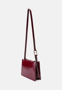 Borsa a tracolla in pelle bordeaux con una forma strutturata, texture liscia, tracolla regolabile e dettagli in metallo dorato.