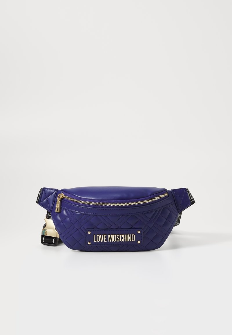 Banane matelassée violette avec quincaillerie en or et plaque logo. Comprend un dessus zippé et une sangle en tissu texturé. Design compact et sportif.