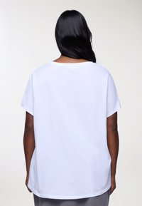 Maglietta di cotone bianca, vestibilità rilassata, maniche corte, scollo rotondo, texture liscia, vista posteriore mostra un orlo curvo e senza grafiche visibili.