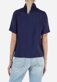 Polo shirt navy a maniche corte con colletto, texture liscia e design leggermente sfiancato, abbinato a jeans a vita alta blu chiaro.