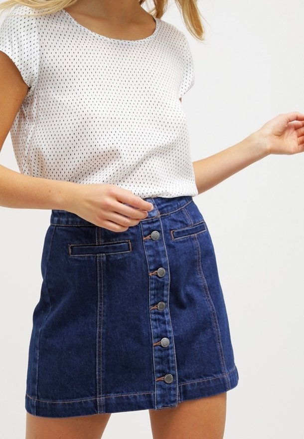 Bílý top s krátkým rukávem a černým tečkovaným vzorem, v kombinaci s modrou džínovou sukní s předními knoflíky a kapsami, strukturovaná látka.