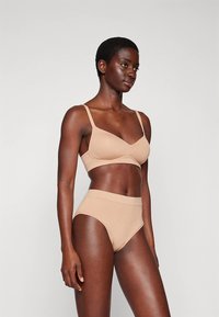 Ensemble soutien-gorge nude et culotte taille haute en tissu lisse et extensible. Design simple avec bretelles réglables et finition sans coutures.