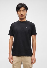 Melnā kokvilnas T-krekls ar īsām piedurknēm. Ar nelielu baltu logotipu krūtīs. Klasiska, apaļa kakla izgriezuma un brīvas formas.