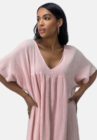 Robe rose pâle à col en V en tissu texturé avec manches courtes larges et détails froncés sous la poitrine.