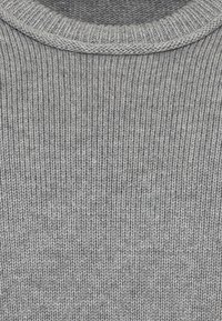 Gros plan sur un pull gris côtelé montrant la texture détaillée et l'encolure arrondie.