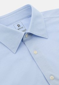 Blå mönstrad skjorta med en klassisk krage, två framknappar och en strukturerad tyg. Varumärkesskylten synlig på insidan.