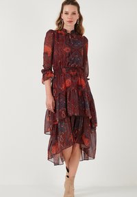Kukallinen paisley-kuosiset mekko pitkillä hihoilla, röyhelöhelmalla ja joustavalla vyötäröllä punaisen, sinisen ja ruskean sävyissä. Läpinäkyvä, kevyt kangas.