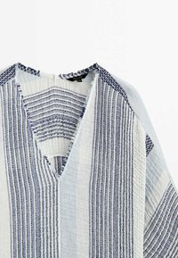 Tissu texturé rayé bleu clair et blanc avec un col en V et des bords effilochés sur un vêtement.