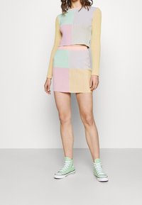 Geribbelde breisels in een twee-delige set bestaande uit een cropped langemouwen top en een mini rok. Kleuren zijn onder andere pastelgroen, roze, geel en paars.