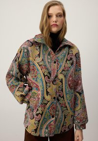 Pisano s potiskom paisleyjev z ovratnikom, gumbi spredaj in dolgimi rokavi. Ponuja zapletene cvetlične vzorce v rdeči, modri, zeleni in rumeni barvi.