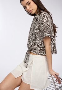 Camicia a maniche corte con stampa zebra marrone e bianca, con un dettaglio a cravatta in vita; abbinata a un pantalone corto relax color crema.