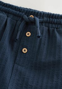 Pantaloni comodi blu navy con tessuto strutturato, dotati di vita elastica, coulisse e quattro bottoni di legno sulla parte anteriore.
