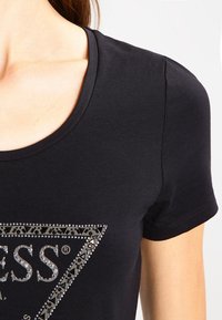 Schwarz, kurzärmeliges T-Shirt mit einem dreieckigen Strassdesign auf der Vorderseite, mit glatter Textur und rundem Halsausschnitt.