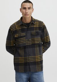 Sort og gul rutet flannel skjorte med to forlommer, knaplukning og krave, der har et tekstureret uldlignende udseende.