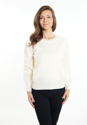 Witte, zachte trui van gebreid materiaal met een ronde halslijn en subtiele versieringen bij de kraag. Lange mouwen, aansluitende taille, gedragen met zwarte broek.