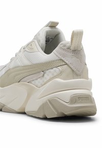 Baskets Puma beige et blanches, axées sur le talon et le côté, avec semelle texturée, tige en mesh, languette et détails du logo.