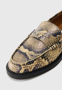 Python-print loafers featuring a smooth, textured surface in beige and black, with a flat black sole and a raised strap across the vamp.