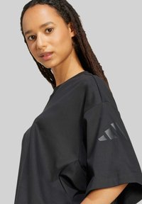 Sort oversized t-shirt med boxy silhuet, korte ærmer og en blank logoaccent på venstre ærme. Glat stofstruktur.
